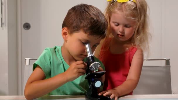 Garçon aide une fille à regarder à travers un microscope — Video