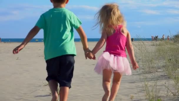 Menino e menina correm pela areia até o mar — Vídeo de Stock