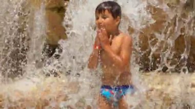 Çocuk havuzdaki kayalıkların üzerinde durarak dans ediyor.