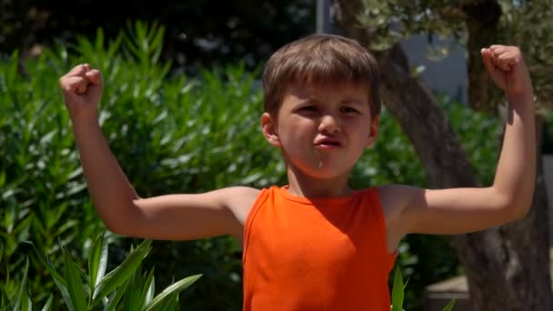 Jongen in een oranje shirt toont spier — Stockvideo
