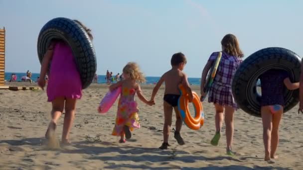 Дети с надувными трубками идут к морю — стоковое видео