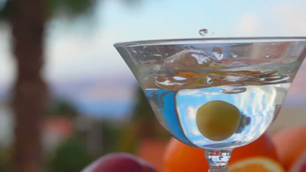 Оливка падает в стакан с мартини на фоне цитрусовых — стоковое видео