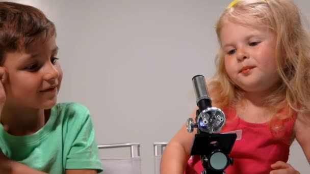 Garçon aide une fille à regarder à travers un microscope — Video