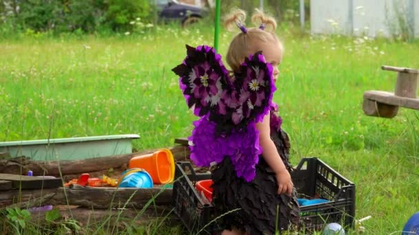 Meisje met vlinder vleugels speelt in de buurt van de zandbak — Stockvideo