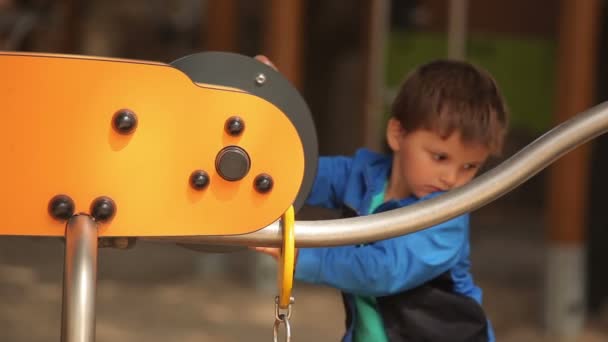 小さな男の子は遊び場でオレンジ色の車輪を回転させます — ストック動画