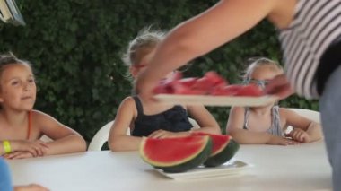 Kadın tarafından getirilen sulu karpuz yiyen çocuklar