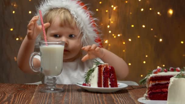 Девушка в красной шляпе Санта-Клауса ест красный бархатный торт — стоковое видео