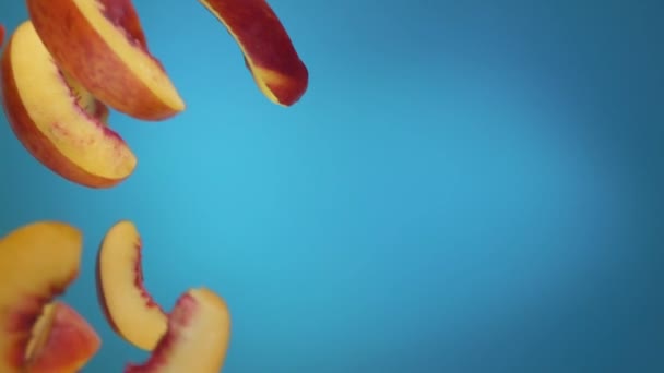 Pfirsichscheiben fliegen auf blauem Hintergrund herunter — Stockvideo