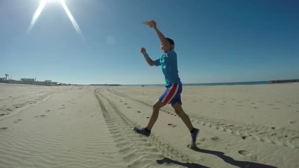 Boy plays with airplane and jumps happily on beach — ストック動画