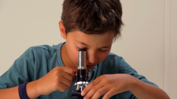 Curieux adolescent brun regarde sérieusement à travers un microscope — Video