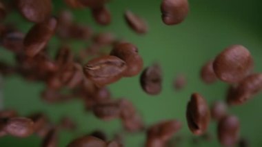Yeşil arka planda uçuşan kavrulmuş kahve çekirdeklerini yakından izleyin.