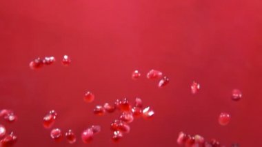 Kırmızı arka planda sulu kırmızı nar taneleri zıplıyor.