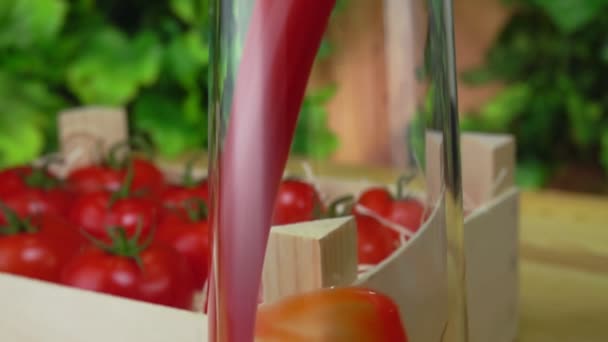 Хвиля томатного соку тече в глечик поруч з дерев'яною коробкою, наповненою помідорами — стокове відео