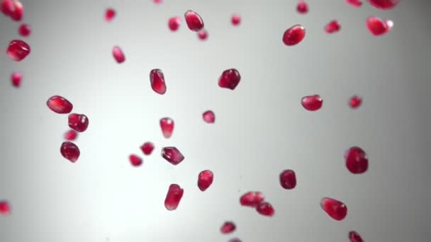 Juicy red grains of ripe pomegranate are flying diagonally on a white background — Stock Video