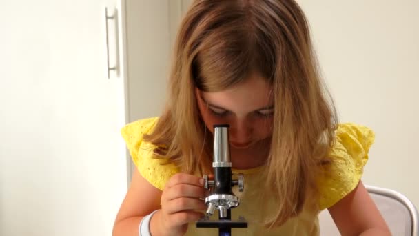 Söt flicka i gul klänning tittar allvarligt genom mikroskopet — Stockvideo