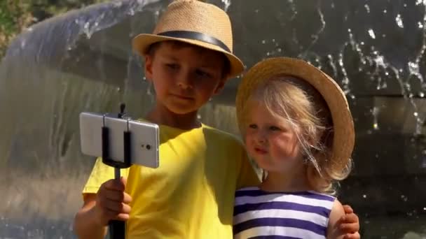 स्ट्रॉ हॅट्समध्ये मुलगा आणि मुलगी फाउंटनच्या पार्श्वभूमीवर सेल्फी बनवत आहेत — स्टॉक व्हिडिओ