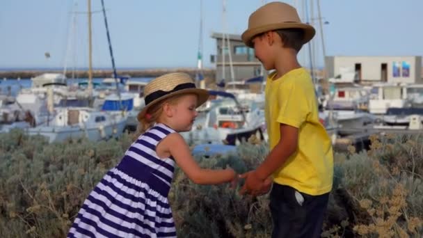 В порту яхты играют прелестные мальчик и девочка в соломенных шляпах — стоковое видео