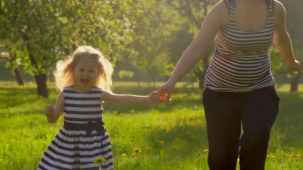 Mamma springer till kameran med sin lilla flicka i den solbelysta äppelträdgården. — Stockvideo