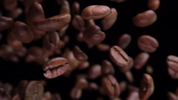 Κοντινό πλάνο των καβουρντισμένων κόκκων καφέ που πετούν και περιστρέφονται στο μαύρο φόντο — Αρχείο Βίντεο