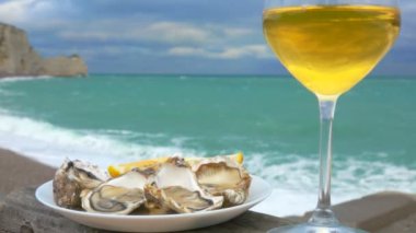 Bir bardak beyaz şarap ve tabakta okyanusun arka planında taze istiridye.