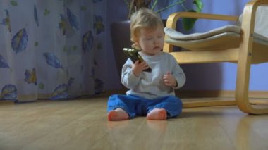 Küçük sevimli bebek bir telefon alıp yerde otururken gülümsüyor.