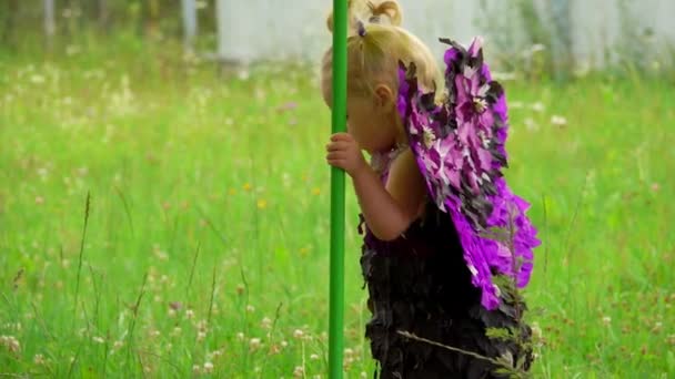 Kleine niedliche blonde Mädchen mit lila Schmetterlingsflügeln geht im Freien
