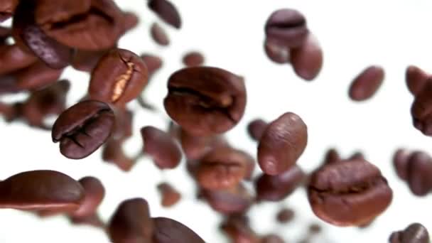 Gros plan des grains de café torréfiés volant et tournant sur le fond blanc — Video