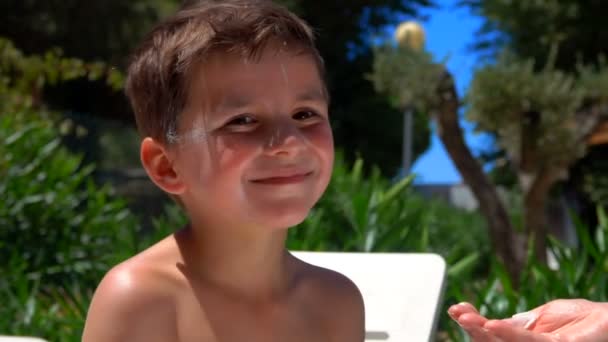 Piccolo abbronzato ragazzo spalmato con una crema di protezione solare sta guardando la fotocamera — Video Stock