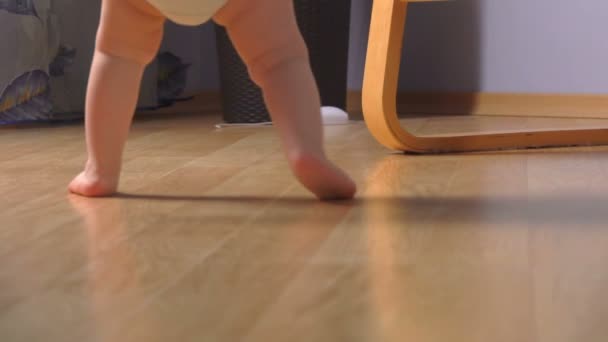 Низкоугольный вид на ноги маленький очаровательный ребенок делает первые шаги — стоковое видео