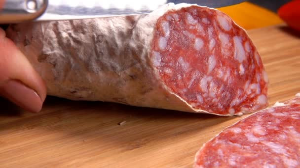 Gros plan de délicieuses saucisses sèches coupées en tranches avec couteau sur une planche de bois — Video