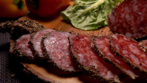 El primer plano de la salchicha seca en hierbas cortadas en rodajas con cuchillo en una tabla de madera — Vídeos de Stock