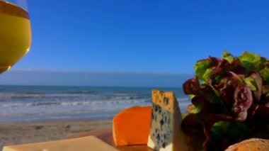 Deniz kenarında çeşitli peynirler, ekmek ve marullarla nefis bir piknik.