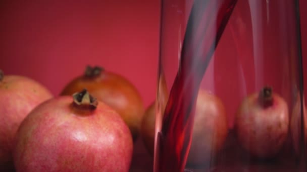 Крупный план красного сока, текущего в стеклянный кувшин на красном фоне — стоковое видео