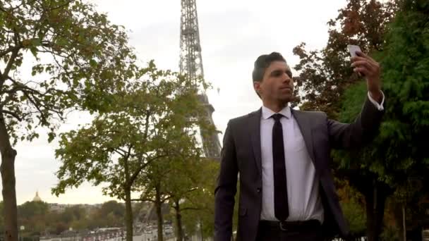 Bonito homem de negócios está fazendo uma selfie no fundo da Torre Eiffel — Vídeo de Stock