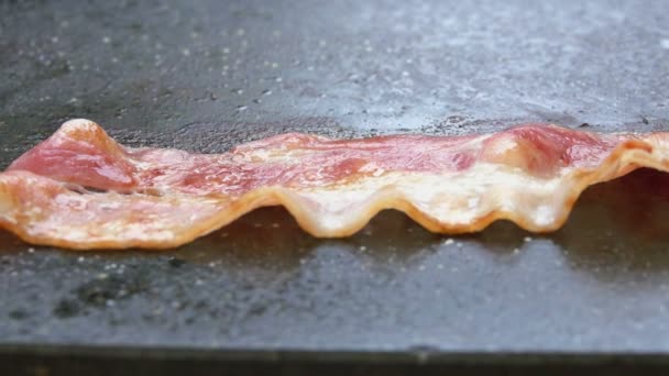 Stekta remsor av bacon rostas på stenytan av den platta grillen — Stockvideo