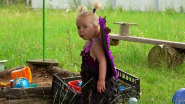 Kelebek kanatlı küçük şirin kız, kum havuzunun yanında oynuyor.