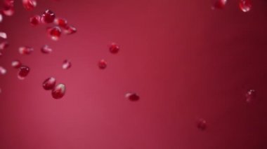 Sulu kırmızı nar taneleri kırmızı arka planda çapraz uçuyor.