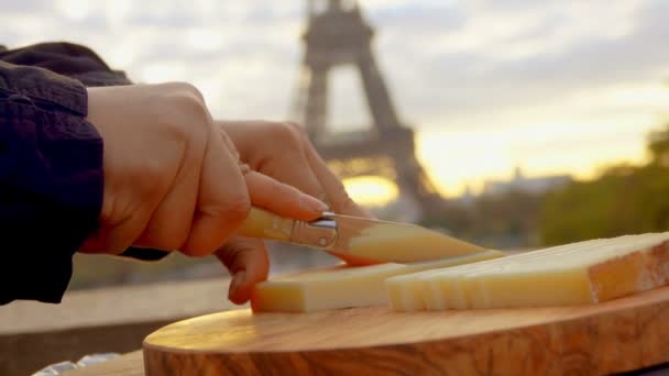 Tangan mengiris keju kambing keras dengan pisau di latar belakang Menara Eiffel — Stok Video