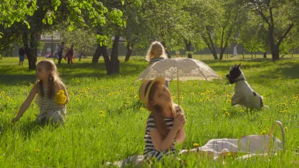 Las niñas están recogiendo flores en el césped y jugando con sombrilla — Vídeos de Stock