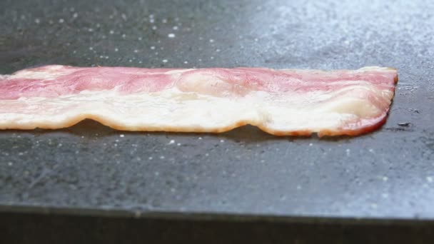 Tunna remsor av bacon vänder på stenytan av den platta grillen — Stockvideo