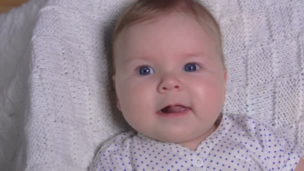 Kleine schattige baby op een witte deken lacht om de camera — Stockvideo