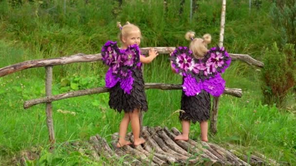 Aranyos szőke lányok lila pillangó szárnyakkal állnak a fa hídon.