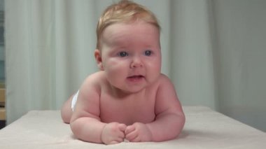 Küçük tombul bebek beyaz bir battaniyenin üzerine uzandı. 
