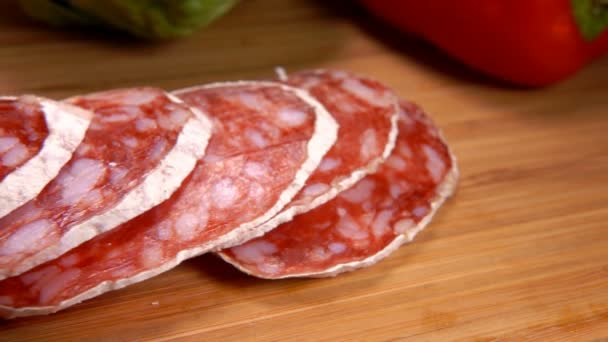 Deliciosas rebanadas de salchicha seca en una piel blanca tomada de una tabla de madera con tenedor — Vídeos de Stock