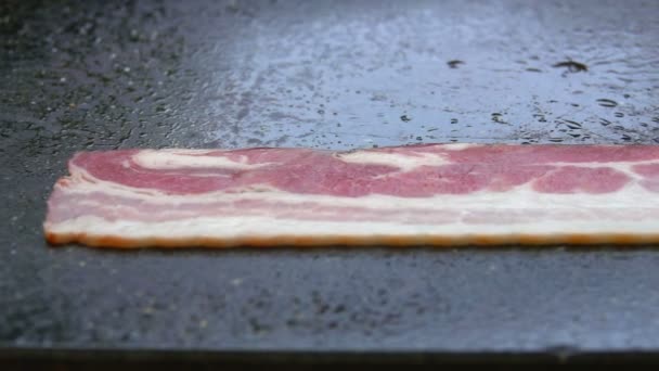 Panorama av en tunn remsa bacon rostning på stenytan av grillen — Stockvideo