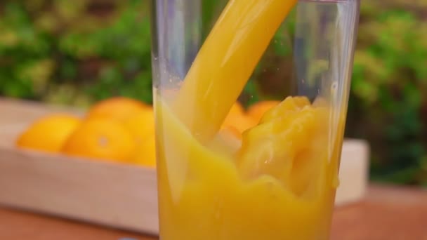El zumo de naranja fresco se vierte en una jarra junto a la caja llena de naranjas maduras — Vídeos de Stock