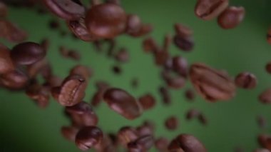 Kavrulmuş Arabika kahve çekirdekleri yakın plan yeşil arka planda çapraz uçuyor.