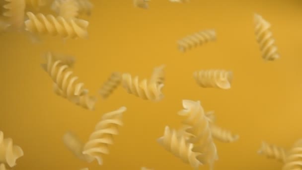 Pastas secas fusili cayendo diagonalmente sobre un fondo amarillo — Vídeo de stock