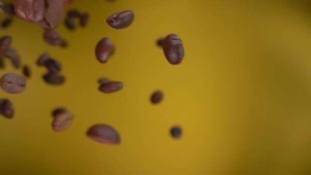 Roasted coffee beans are flying diagonally on the ochre yellow background — Stock Video