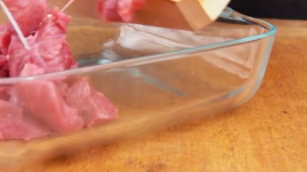 Kawałki pokrojonego surowego mięsa spadają z drewnianej deski do szklanej tacy. — Wideo stockowe